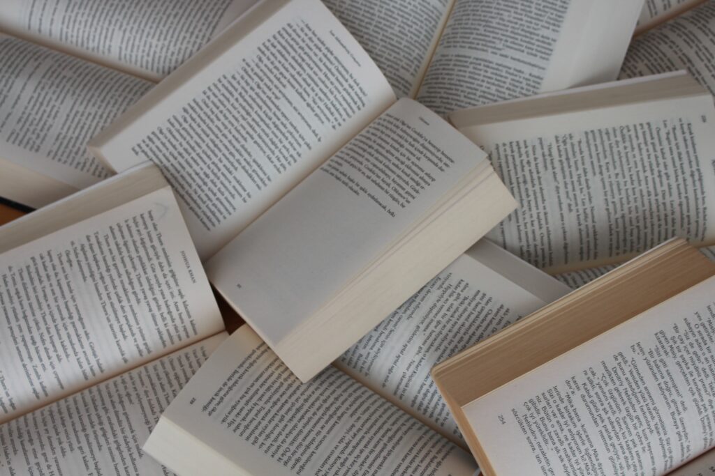 A stack of books overlapping each other, all open, with black text on white pages.