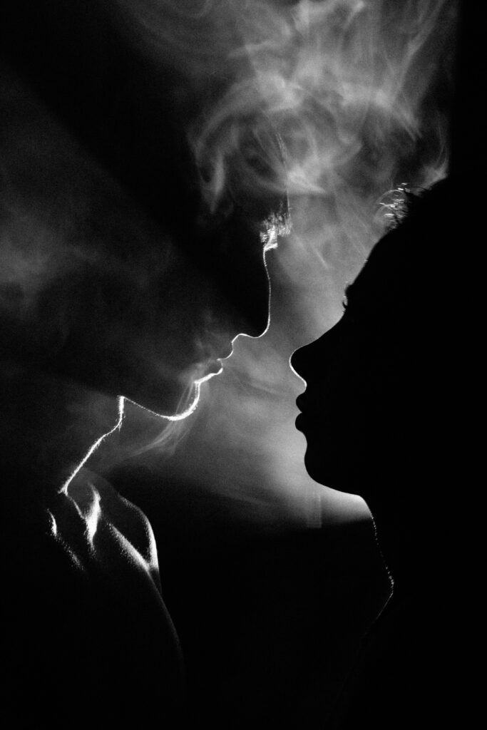 A man and a woman looking at each other in sihouette, so that their profiles are visible but not much else, with smoke rising in between them.